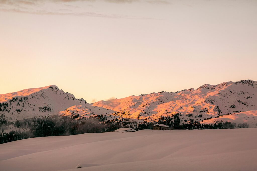 Peaceful winter scene with snow-covered mountains at sunrise, highlighting tranquil beauty.